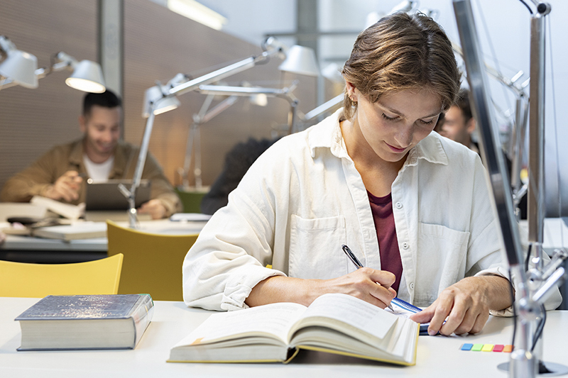 Studentin arbeitet konzentriert mit einem Buch in der Bibliothek.