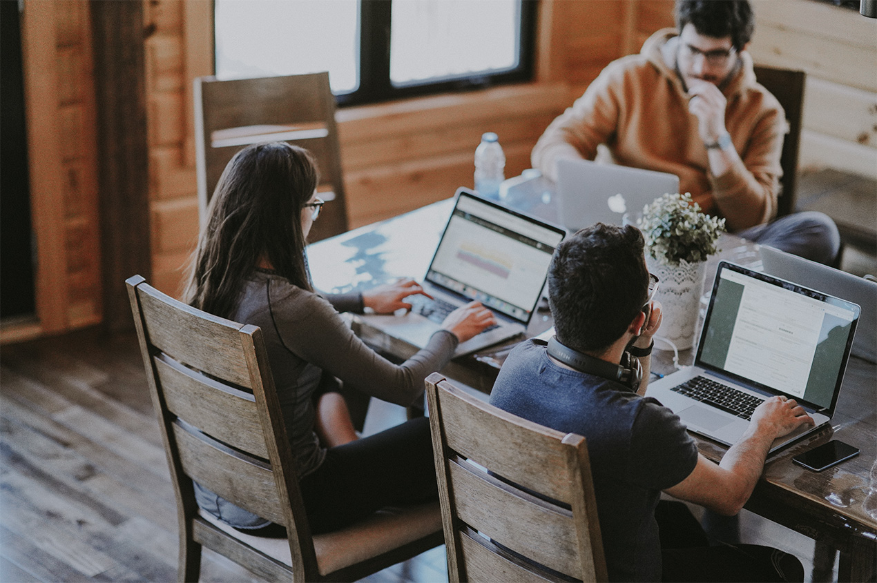 Drei Personen sitzen an einem Schreibtisch mit Laptops