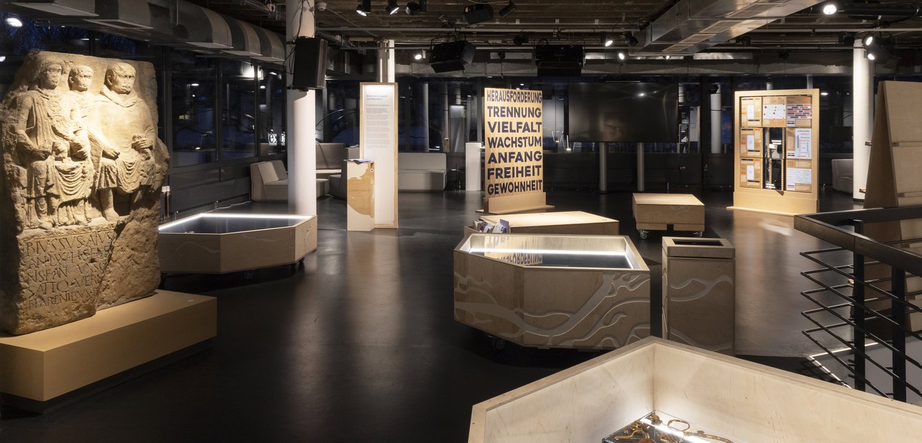 Ausstellung zu Migration mit antikem Steinrelief und interaktiven Stationen