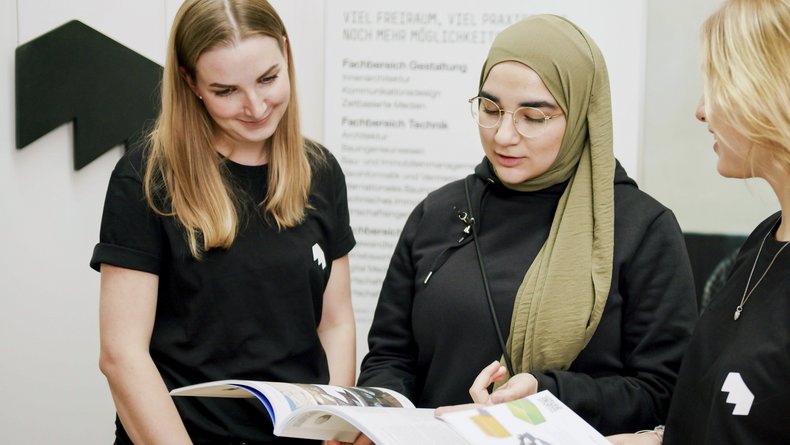 Mitarbeitende der Allgemeinen Studienberatung informieren Studieninteressierte an einem Messestand der Hochschule Mainz über Studienmöglichkeiten und Studiengänge.