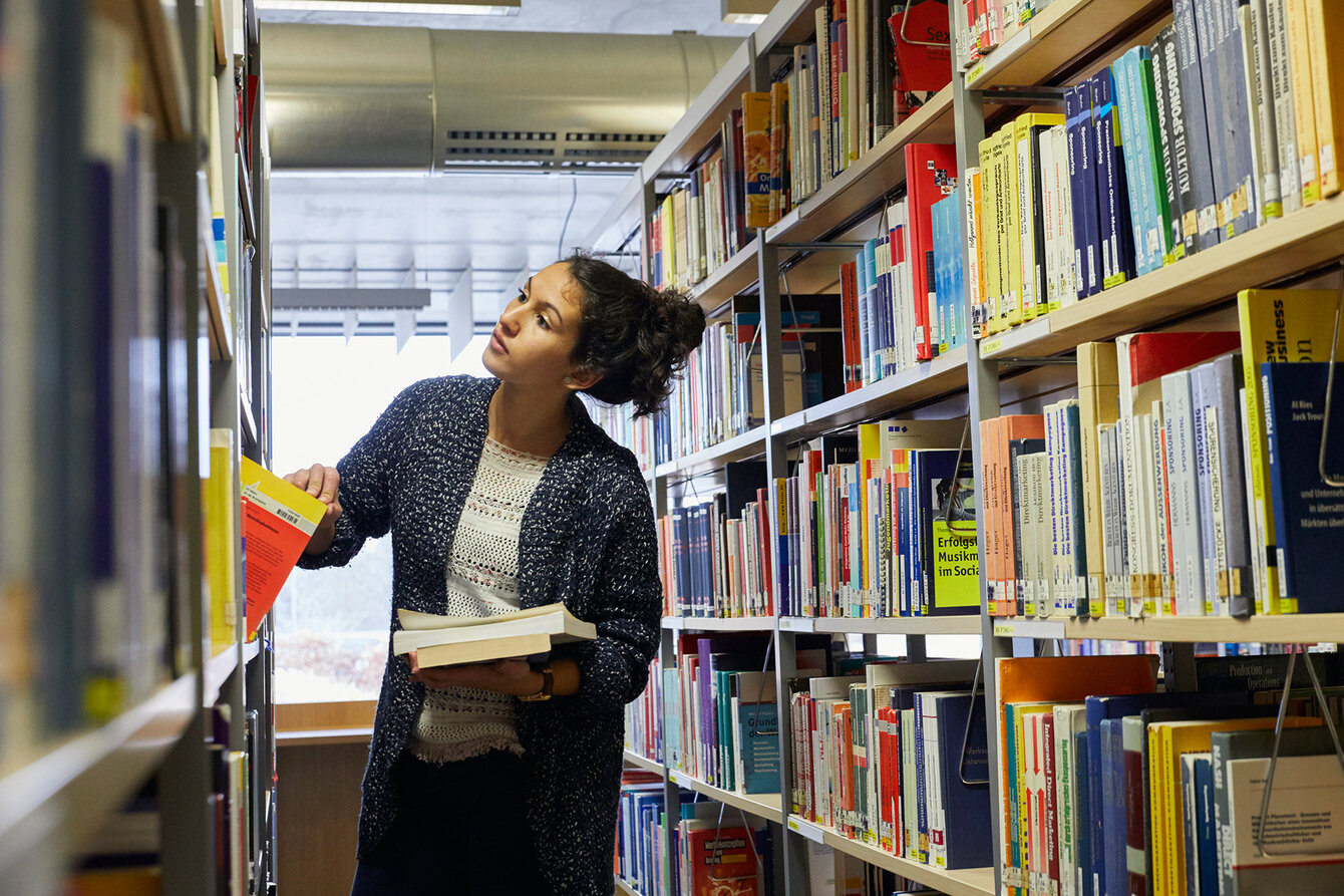 Studentin nimmt Buch aus Bücherregal