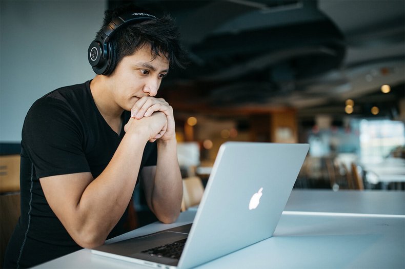 Eine Person sitzt mit Kopfhörern an einem Tisch und guckt konzentriert auf einen Laptop.